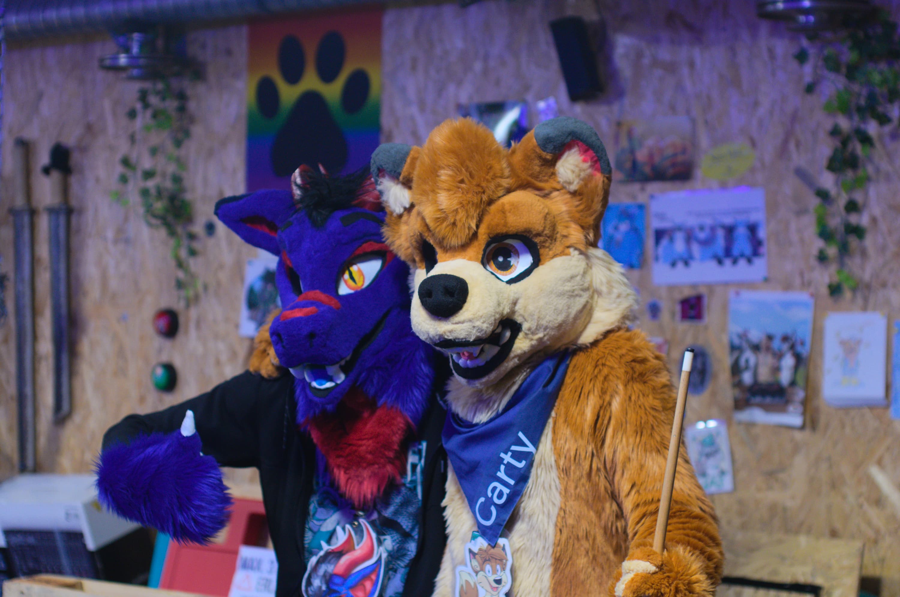 A blue dragon fursuit holding another fursuit in their arm, both holding pool cues.